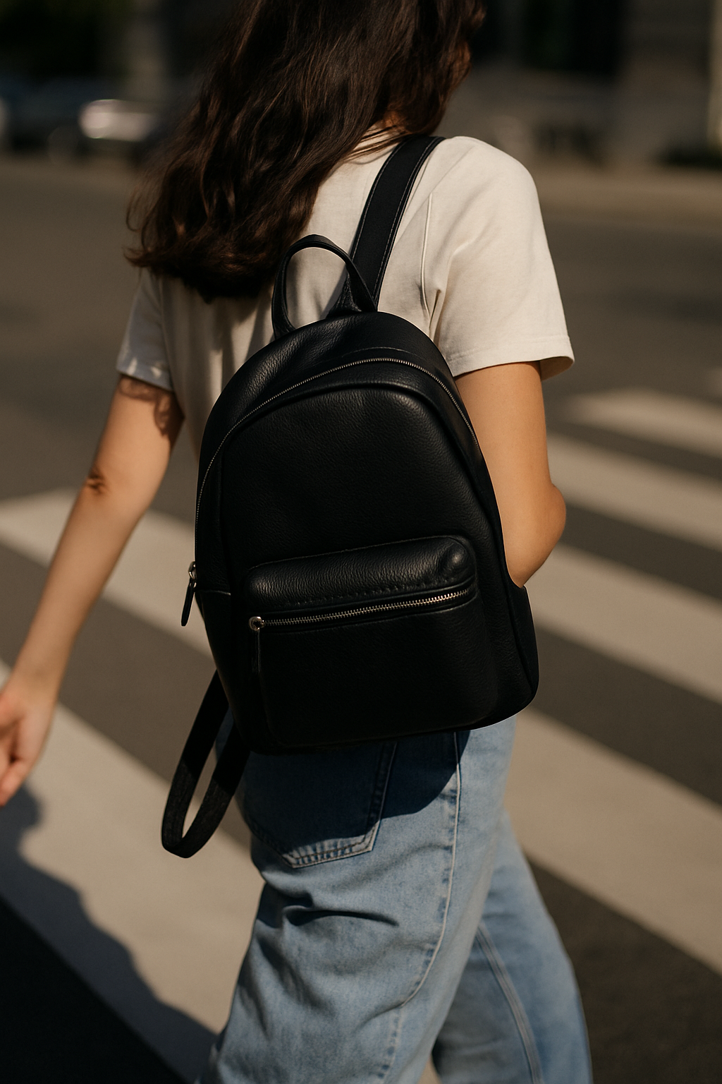 Black leather backpack worn over one shoulder in city street
